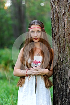 A young beautiful Slavic girl with long hair and Slavic ethnic dress stands in a summer forest with a ritual dagger in her hands