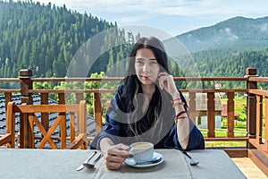 Young, beautiful, sleepy woman drinks coffee on a background of mountains in the early morning