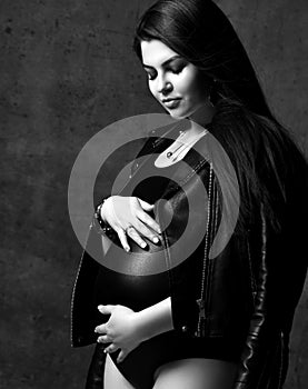 Young beautiful slim pregnant woman with long hair in black body and leather jacket. Pregnancy fashion look concept