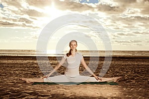 Young beautiful slim woman practices yoga on the beach at sunrise. Yoga at sunset