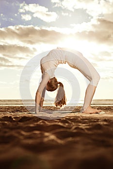 Young beautiful slim woman practices yoga on the beach at sunrise. Yoga at sunset