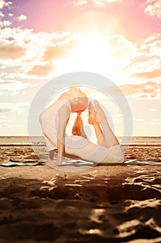 Young beautiful slim woman practices yoga on the beach at sunrise. Yoga at sunset