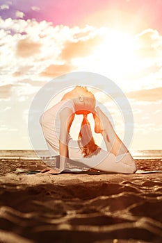 Young beautiful slim woman practices yoga on the beach at sunrise. Yoga at sunset