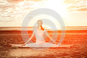 Young beautiful slim woman practices yoga on the beach at sunrise. Yoga at sunset