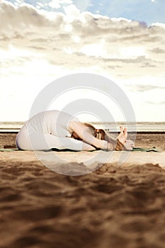 Young beautiful slim woman practices yoga on the beach at sunset