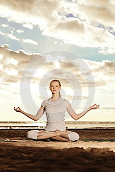 Young beautiful slim woman practices yoga on the beach at sunset