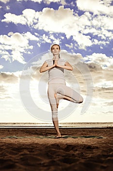 Young beautiful slim woman practices yoga on the beach at sunset