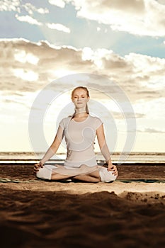 Young beautiful slim woman practices yoga on the beach at sunset