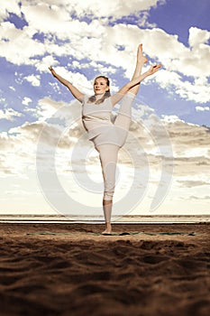 Young beautiful slim woman practices yoga on the beach at sunset