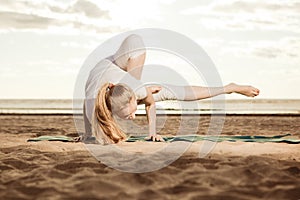 Young beautiful slim woman practices yoga on the beach at sunset