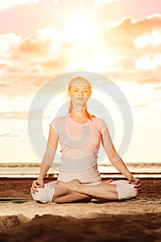 Young beautiful slim woman practices yoga on the beach at sunset