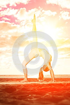 Young beautiful slim woman practices yoga on the beach at sunset