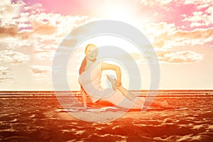 Young beautiful slim woman practices yoga on the beach at sunset