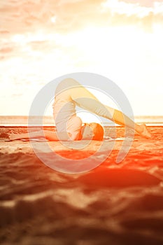 Young beautiful slim woman practices yoga on the beach at sunset