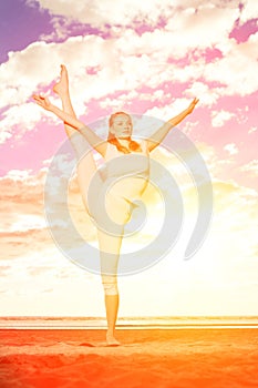 Young beautiful slim woman practices yoga on the beach at sunset