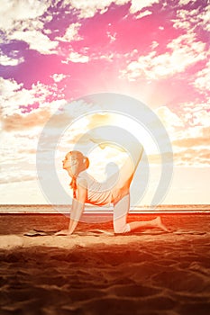 Young beautiful slim woman practices yoga on the beach at sunset