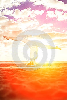 Young beautiful slim woman practices yoga on the beach at sunset