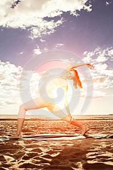 Young beautiful slim woman practices yoga on the beach at sunset