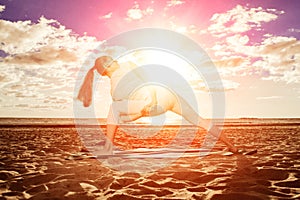 Young beautiful slim woman practices yoga on the beach at sunset