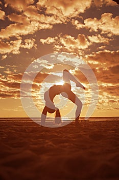 Young beautiful slim woman silhouette practices yoga on beach