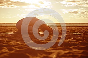 Young beautiful slim woman silhouette practices yoga on the beach at sunrise. Yoga at sunset