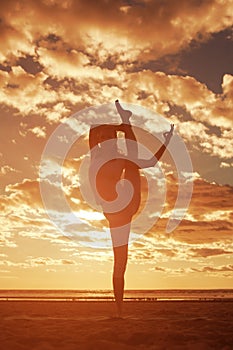 Young beautiful slim woman silhouette practices yoga on the beach at sunrise. Yoga at sunset