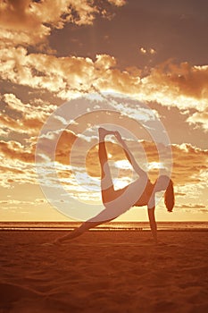 Young beautiful slim woman silhouette practices yoga on the beach at sunrise. Yoga at sunset