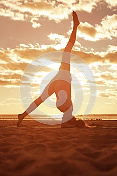 Young beautiful slim woman silhouette practices yoga on the beach at sunrise. Yoga at sunset