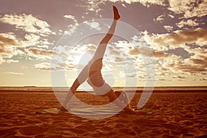 Young beautiful slim woman silhouette practices yoga on the beach at sunset. Yoga at sunrise