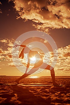 Young beautiful slim woman silhouette practices yoga on the beach at sunset. Yoga at sunrise