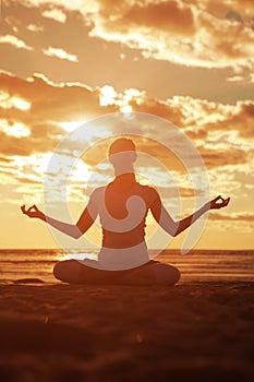 Young beautiful slim woman silhouette practices yoga on the beach at sunset. Yoga at sunrise