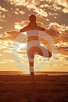 Young beautiful slim woman silhouette practices yoga on the beach at sunset. Yoga at sunrise