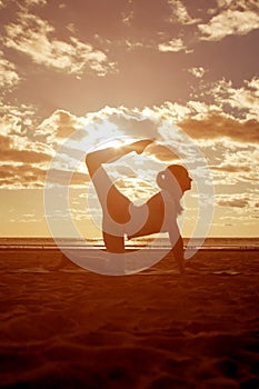 Young beautiful slim woman silhouette practices yoga on the beach at sunset. Yoga at sunrise