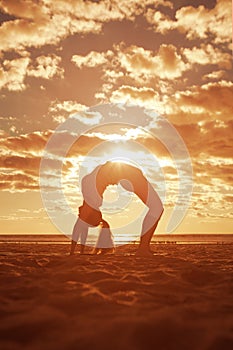 Young beautiful slim woman silhouette practices yoga on the beach at sunset. Yoga at sunrise