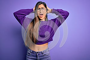 Young beautiful smart woman wearing glasses over purple isolated background Crazy and scared with hands on head, afraid and