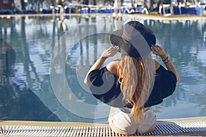 Young beautiful smile girl in black fashion hat, red lips and long hair, posing near pool beackground of palms.