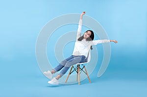 Young beautiful smiling asian girl relaxing sitting on chair isolated on blue background