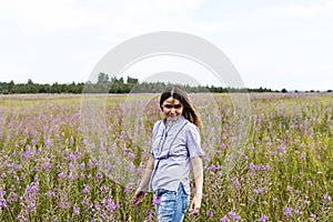 Young beautiful smiling blond woman in purple shirt walking in the meadow among flowers of fireweed