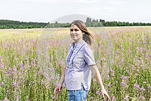 Young beautiful smiling blond woman in purple shirt walking in the meadow among flowers of fireweed