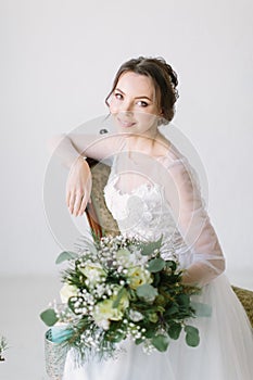 Young beautiful smiling bride with bouquet of flowers sitting in a chair , close-up