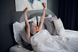 Young beautiful smiling and brunette woman lying in bed trying to wake up early morning stretching hands after sleep photo