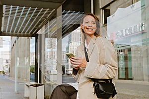 Young beautiful smiling business woman holding phone and looking aside