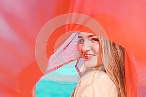 Young beautiful smiling caucasian blond woman, with minimal makeup, in light dress and red thin scarf against blue sky