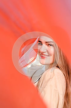 Young beautiful smiling caucasian blond woman, with minimal makeup, in light dress and red thin scarf against blue sky