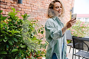 Young beautiful smiling curly woman hodling phone looking on it