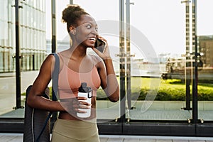 Young beautiful smiling fit afro woman talking phone holding bottle