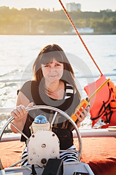 Young beautiful smiling girl in dress sailing luxury yacht in sea with walkie-talkie in hands, sunset