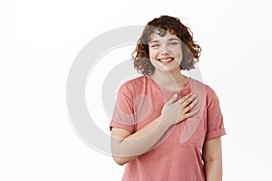 Young beautiful smiling girl holding one hand on heart, looking happy and heartfelt, being touched by something