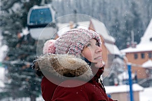 Young beautiful smiling girl looking sideways in pink knitted hat with pompon and white mittens with pattern in warm jacket of