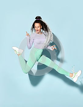 Young beautiful smiling girl with modern hairstyle in sportswear and sneakers jumping with legs stretched out